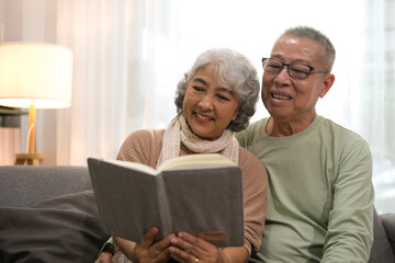 Happy smiling senior family couple in love reading book together, hugging embracing while spending...