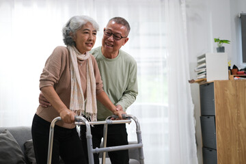 Elderly man helping his wife with walking frame indoors