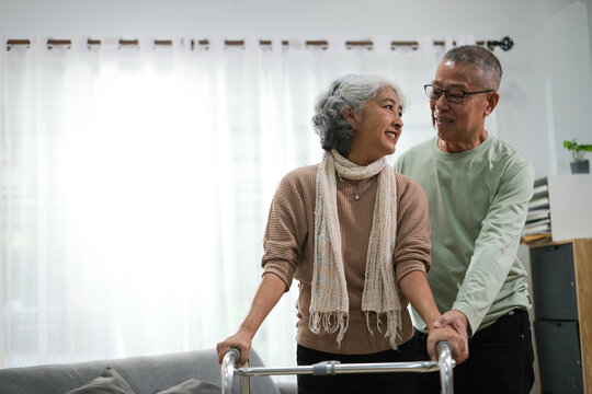 Elderly man helping his wife with walking frame indoors