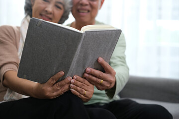 Happy smiling senior family couple in love reading book together, hugging embracing while spending...