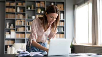 Housewife leaned over table typing message on pc order goods online do household chores, busy...
