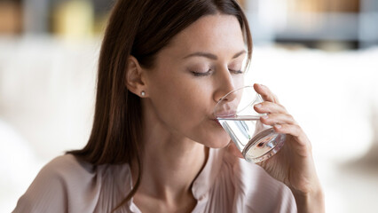 Close up thirsty 30s woman holding transparent glass drinking enough daily dose still water...