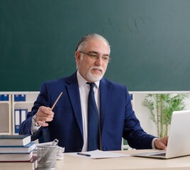 Aged male teacher in front of chalkboard