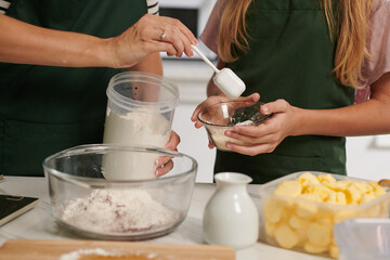 Closeup image of mother showing daughter how much flour she should put in bowl when making dough