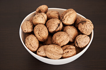 Whole walnuts in a white plate on a dark background. Close-up