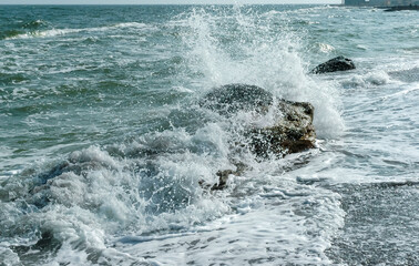 Sea waves crashing against rocks on a sand and stone beach