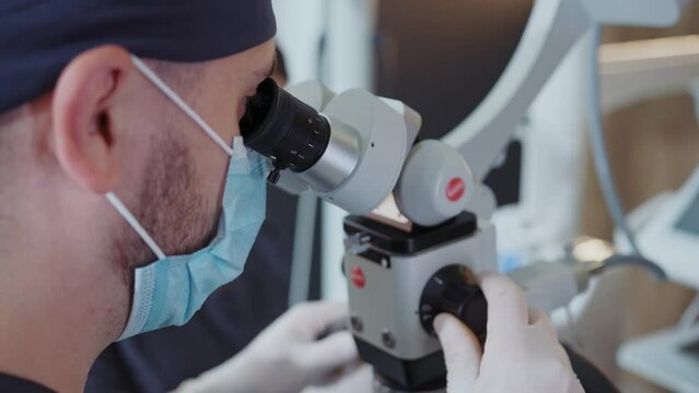 Close-up shot of dentist in uniform looking at dental operating microscope hi-res. Doctor using medical equipment. Medicine and healthcare concept