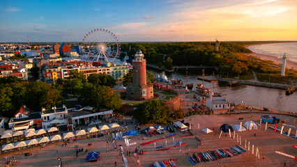 Kolobrzeg town at sunset. Ferris wheel, lighthouse, harbour and sandy beach. Taken from a drone. Kołobrzeg is a city in Poland. - obrazy, fototapety, plakaty