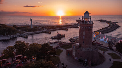 A lighthouse at sunset. The harbour and the Baltic Sea in the background of Kolobrzeg. Taken from a drone. Kołobrzeg is a city in Poland. - obrazy, fototapety, plakaty