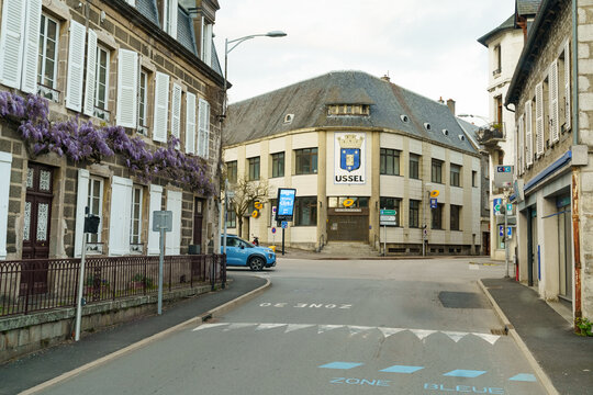 A road lined with houses and parked cars in a French town.