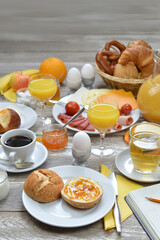 breakfast table with lots of fresh food like coffee, rolls, cheese, eggs, orange juice, tea, jam, butter, banana, apple, orange and a basket full of croissant, rolls and pretz with copy space to above