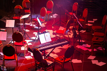 Musical instruments of symphonic orchestra and music stands for music on concert stage after concert. Notes are lying on the floor