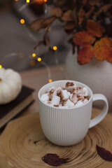  a white cup of coffee with marshmellow on wooden board,Little white pumpkin, lights, vase with leaves. 