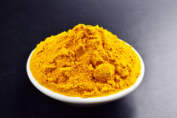 Closeup of turmeric powder in bowl on dark background
