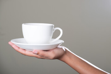 Cup of tea with saucer in hand on grey background