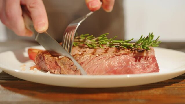 Man eats beef steak medium rare doneness for dinner cutting off piece of meat with knife close-up.