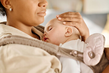 Close-up of young mother lullabying her baby in sling