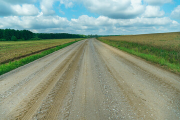 Naklejka premium A dry sandy road passes through a field under the scorching sun and clouds. Dirt road outside the city in the village. Arid climate on earth. Climate change and its consequences.