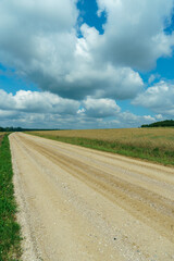 A dry sandy road passes through a field under the scorching sun and clouds. Dirt road outside the city in the village. Arid climate on earth. Climate change and its consequences.