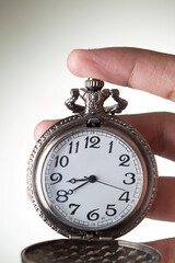 Closeup of pocket watch in hand on grey background