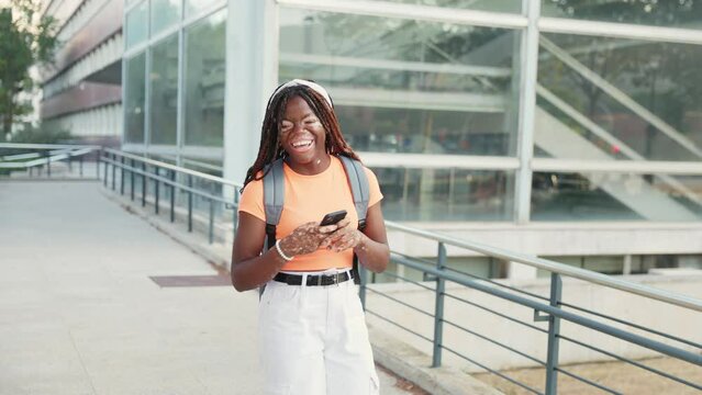 Teenage student girl walking around campus using mobile phone while smiling