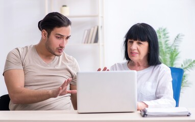 Young male employee explaining to old female colleague how to us