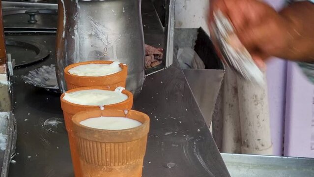 man adding cream malai to lassi churned milk buttermilk drink popular in jaipur, chandigarh, punjab, haryana, rajasthan traditionally served in earthenware terracota glasses