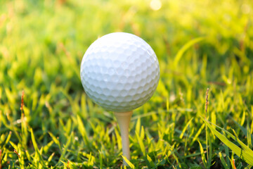 Golf ball set on tee with green, yellow bokeh background and fairy lights