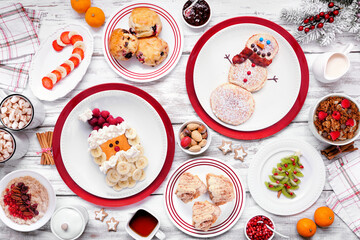Christmas breakfast table scene. Above view on a white wood background. Fun holiday food concept. Santa and snowman pancakes, scones, fruit and cereals.