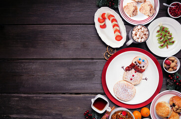 Fototapeta na wymiar Christmas breakfast side border. Top view on a rustic dark wood background. Fun holiday food concept. Snowman pancakes, scones, fruit and cereal. Copy space.
