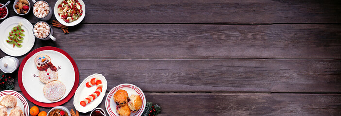 Christmas breakfast corner border. Top view on a rustic dark wood banner background. Fun holiday food concept. Snowman pancakes, scones, fruit and cereals. Copy space.