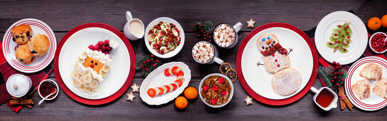Christmas breakfast table scene. Above view on a rustic dark wood banner background. Fun holiday food concept. Santa and snowman pancakes, scones, fruit and cereals. - obrazy, fototapety, plakaty