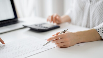 Two accountants using a laptop computer and calculator for counting taxes at white desk in office. Teamwork in business audit and finance