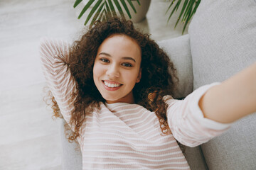 Close up young woman wear casual clothes lay down on grey sofa couch do selfie shot pov mobile cell phone stay at home hotel flat rest relax spend free spare time in living room indoor Lounge concept