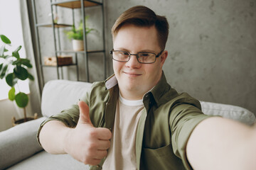 Young man with down syndrome wears casual clothes do selfie shot on mobile cell phone sits on grey...