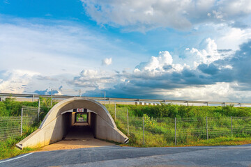 View of tunnel for cars passing under a motorway with a grassy hill and beautiful sky in...