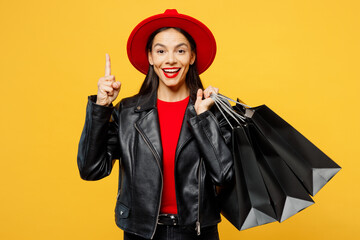 Young insighted woman wear casual clothes red hat hold shopping paper package bags holding index finger up with great new idea isolated on plain yellow background. Black Friday sale buy day concept.