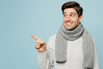 Young ill sick man wear gray sweater scarf point index finger aside on area isolated on plain blue...