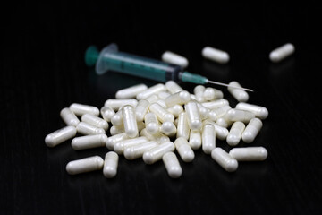 White pills and syringe on a black wooden table, medication in capsules. Background for pharmacy,...