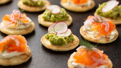 Mini blini pancakes with soft cheese, cold smoked salmon and guacamole