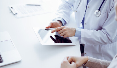 Doctor and patient sitting at the table in clinic. The focus is on female physician's hands using...