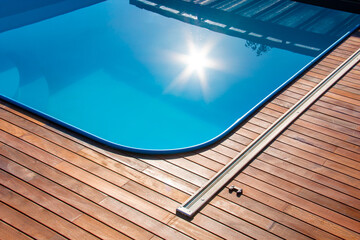 Ipe wood decking around the pool, edge of the outdoor swimming pool with sun reflection on the blue water - obrazy, fototapety, plakaty