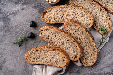 Baked sourdough bread from whole grain flour and pumpkin seeds on a grid, olive oil and black olive on a rustic wooden table. Artisan bread.