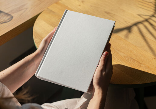 Book mock up, hand holding hard cover mockup on wood table