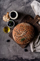 Baked sourdough bread from whole grain flour and pumpkin seeds on a grid, olive oil and black olive on a rustic wooden table. Artisan bread.