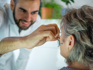 Young audiologist helping to insert an electronic hearing aid to an old woman patient