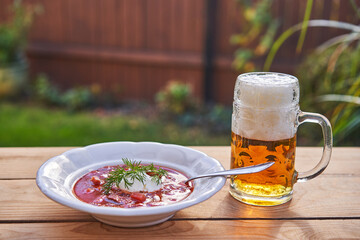 Traditional homemade borsch soup served in deep plate and silver spoon in garden with mug of czech pilsner beer. Healthy and satisfying dish with balanced nutritions served like main course for lunch.