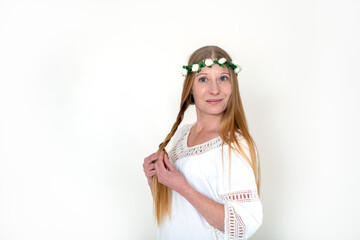 The innocent image of a young woman with long hair in a rose wreath and a white dress on a white background in the studio. Purity, harmony, identity and femininity.