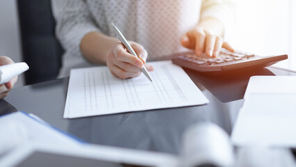 Woman accountant using a calculator and laptop computer while counting taxes with a client or colleague. Business audit team