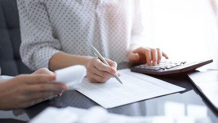 Woman accountant using a calculator and laptop computer while counting taxes with a client or...